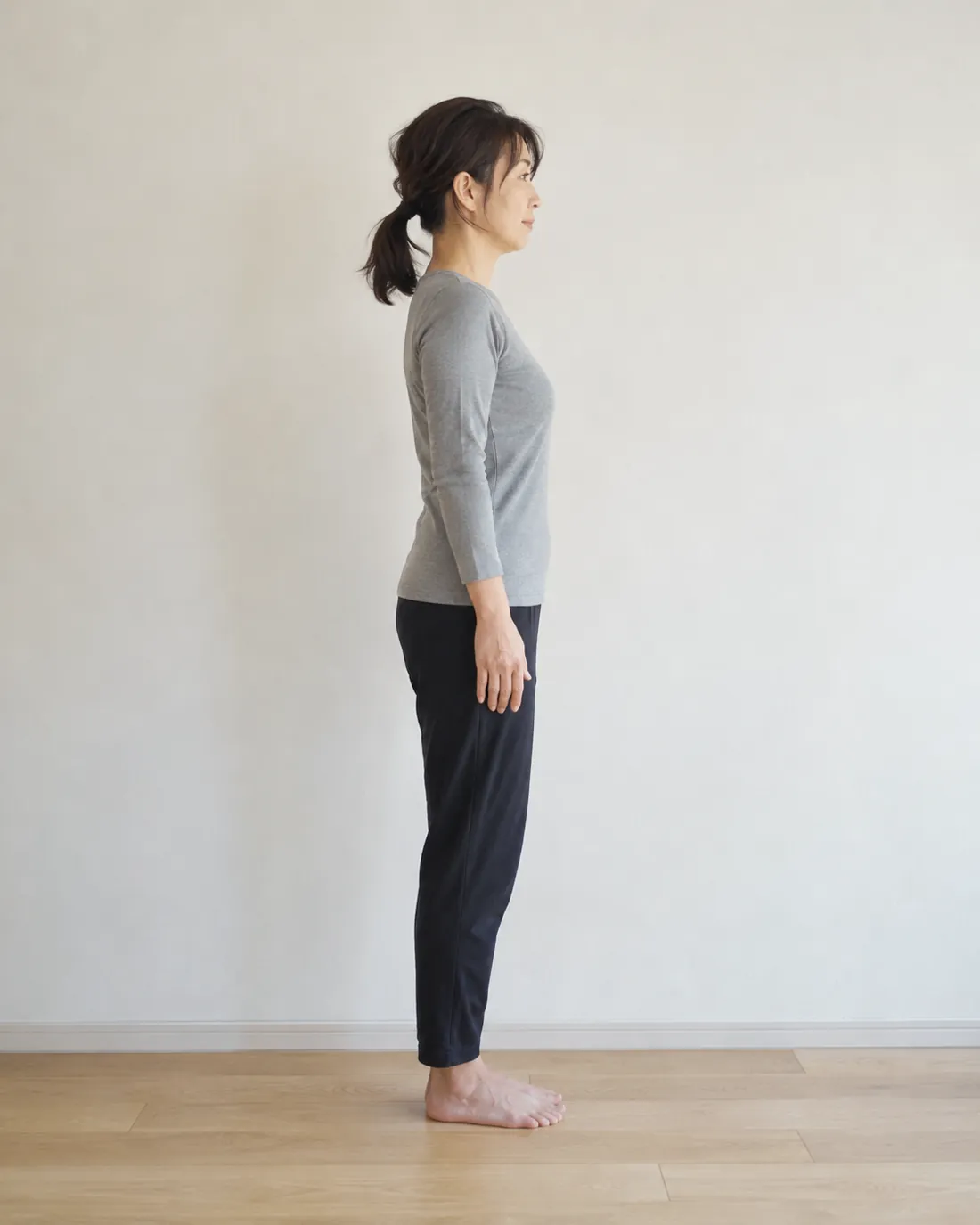 白い壁の前で、横向きに自然に立つ女性