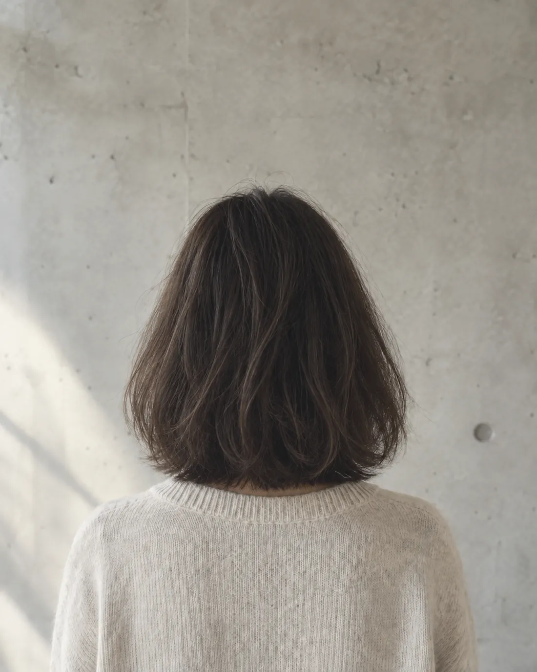 カット前。肩までの髪が、毛先にかけて重く横に広がっている後ろ姿