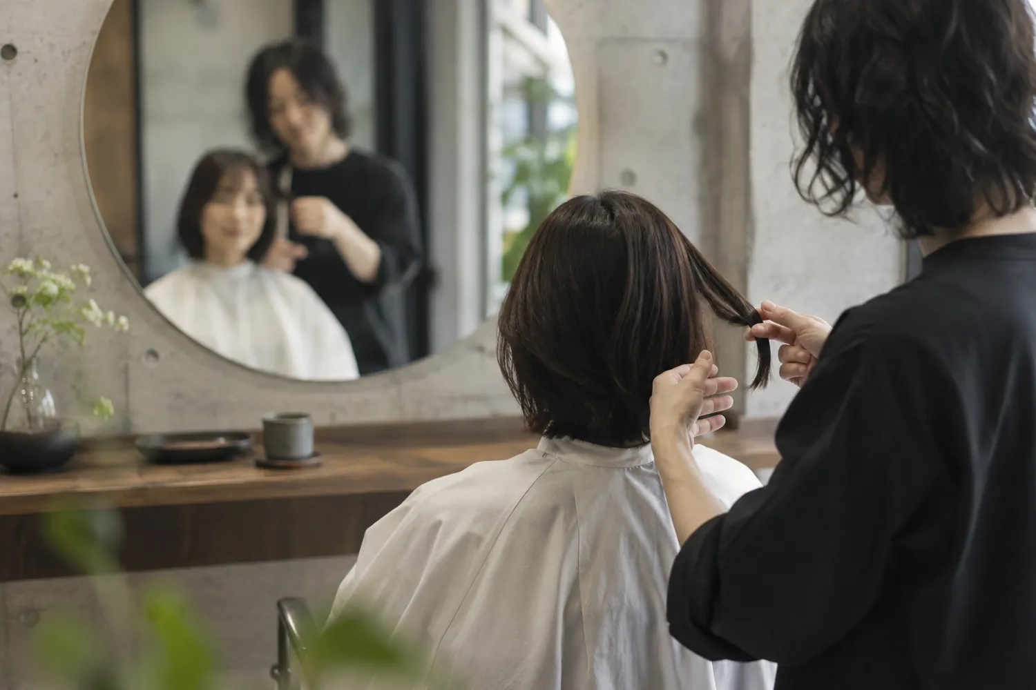 鏡越しに、毛先の重さを手で確かめながら話すスタイリスト